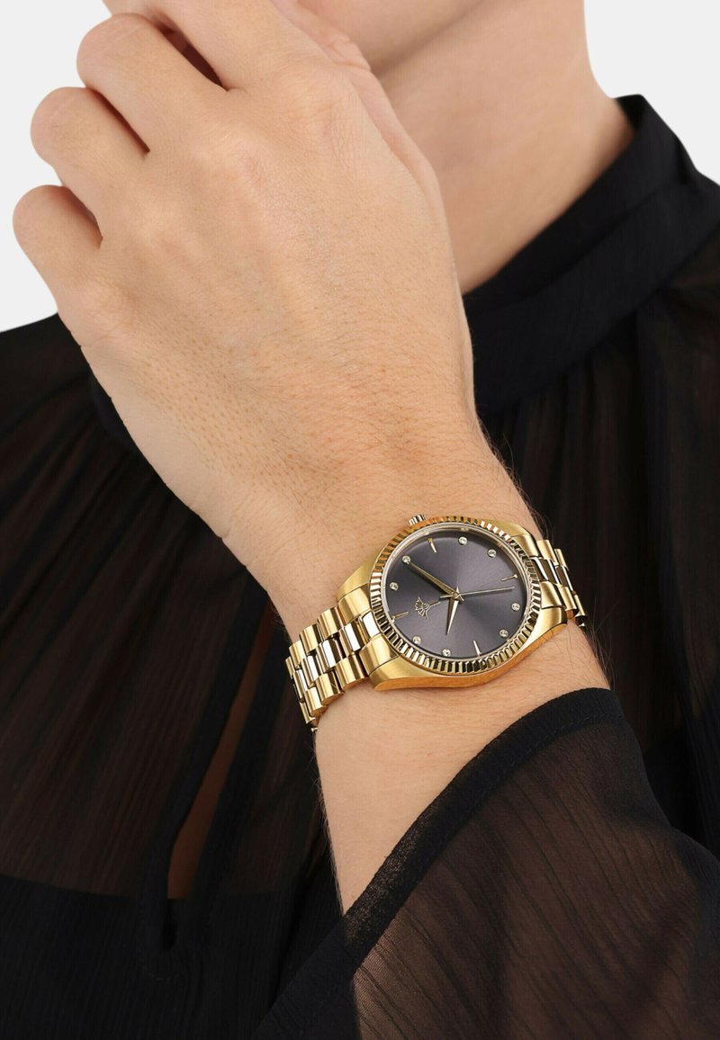 Goldene Uhr mit rundem Ziffernblatt, grauem Zifferblatt und silberfarbenen Zeigern. Verfügt über ein gemustertes Gliederarmband und dekorative Akzente am Lünette.