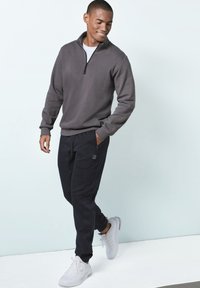 Gray zip-up sweatshirt in soft fabric, paired with black tapered sweatpants featuring side pockets. White athletic sneakers complete the look.