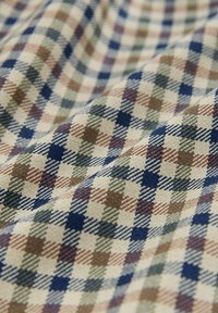 Gros plan d'un tissu doux avec un motif à carreaux beige, bleu, marron et vert et des plis visibles dans la texture.