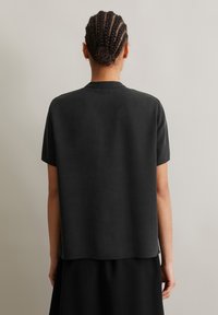 Kurze Ärmel, schwarzes Shirt aus glattem Stoff, mit einem runden Halsausschnitt und lockerer Passform, geradem Saum und minimalen Details.