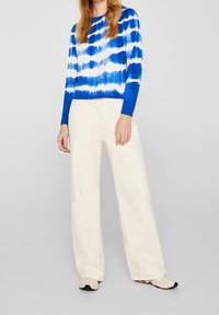 Sinivalkoraidallinen pitkähihainen neule pyöreällä pääntiellä, yhdistetty leveälahkeisiin kermaan sävyisiin housuihin ja beigen värisiin kenkiin. Sileä pinta.