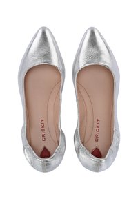 Blanco metallizzato piatto con punta appuntita e ritagli arrotondati sul tallone. Texture liscia con un morbido interno beige e logo rosso.