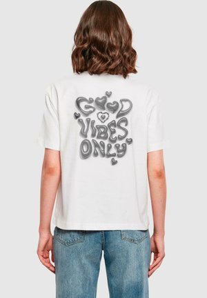 Hvit bomulls t-skjorte med grafisk design på baksiden, med teksten "GOOD VIBES ONLY" i grått og hjerteaccent. Korte ermer, avslappet passform.
