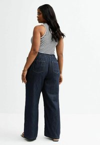Pantalons en denim foncé à jambes larges avec une coupe décontractée et une ceinture élastique, associés à un débardeur noir et blanc à rayures.