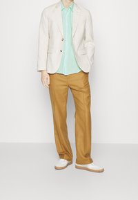 Jasno beżowa lniana marynarka, miętowa koszula na guziki i beżowe spodnie. Białe trampki z beżowymi podeszwami. Prosty, dopasowany krój.