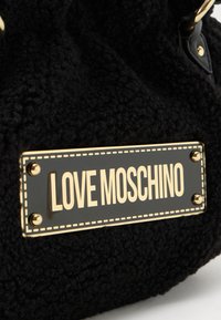 Black textured bag with a rectangular metal plate displaying "LOVE MOSCHINO" in gold letters, secured by four gold screws.