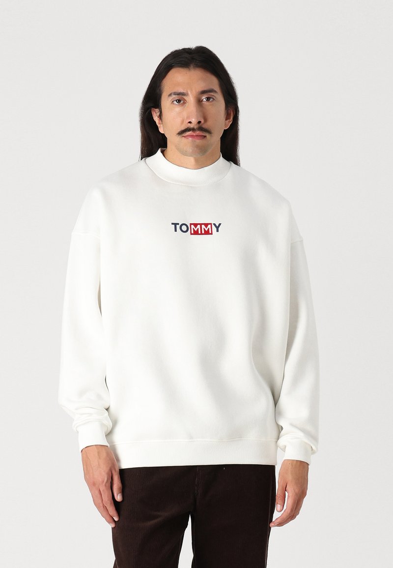Fehér pulóver magas nyakkal, a mellkason kék és piros "TOMMY" logóval. Puha tapintású és lazán illeszkedő ujjak.