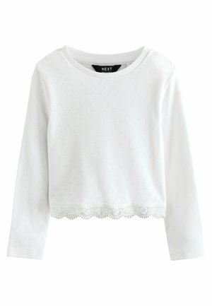Haut à manches longues blanc avec un col rond, présentant un motif texturé, une finition en dentelle à bords festonnés à l'ourlet, et en tissu coton doux.