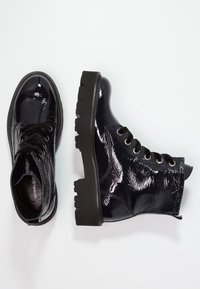 Bottines noires en cuir verni avec une semelle en caoutchouc noir épaisse, bout rond et design à lacets ; comporte une surface texturée et des œillets.