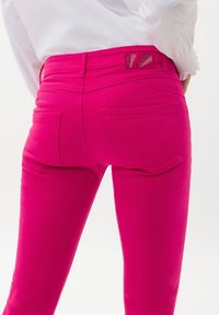 Světlé růžové džíny s těsným střihem, obsahující dvě zadní kapsy a detaily na pásku. Hladká textura a žádné viditelné kovové prvky.