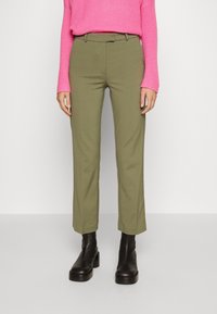 Pantaloni su misura verde oliva con gamba dritta, passanti per cintura e tasche laterali, abbinati a un maglione strutturato rosa brillante e stivaletti neri alla caviglia.