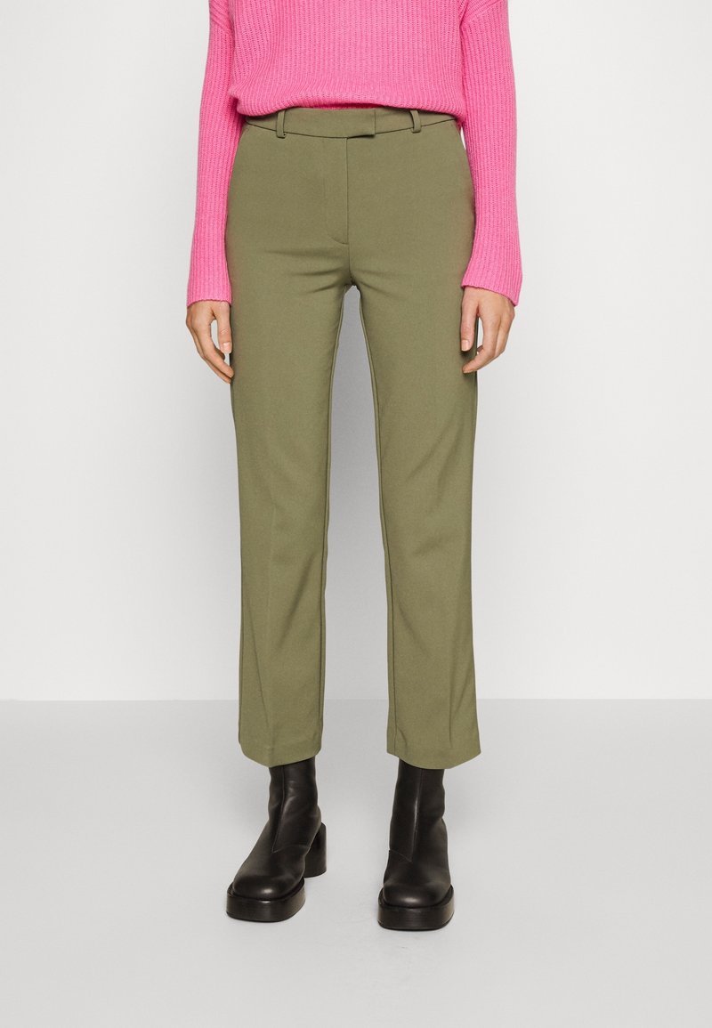 Pantaloni su misura verde oliva con gamba dritta, passanti per cintura e tasche laterali, abbinati a un maglione strutturato rosa brillante e stivaletti neri alla caviglia.