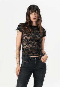 Μαύρο μπλουζάκι από δαντέλα με κοντά μανίκια, με λουλουδάτο σχέδιο και εφαρμοστή γραμμή, συνδυασμένο με σκούρα τζιν παντελόνι.