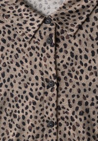 Chemise marron avec des taches irrégulières noires et brun foncé, avec un col et quatre boutons noirs sur le devant.