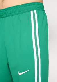 Green athletic shorts made of mesh fabric, featuring white side stripes and a small white Nike logo on the front. Elastic waistband included.