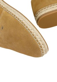 Chaussures en suède marron à enfiler avec des accents tissés beige le long de la semelle, présentant un bout arrondi et une semelle en caoutchouc texturé pour une meilleure adhérence.