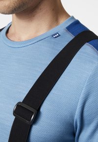 Modrá technická košile s texturovaným povrchem, která má černý nastavitelný popruh upevněný obdélníkovou sponou. Malé logo na límci.