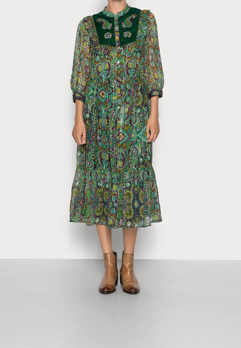 Robe verte à motif cachemire avec col à volants, fermeture à boutons et manches longues. Haut en velours. Bottines marron.