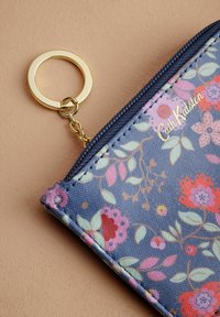 Cvečka torbica v temno modri prevleki, okrašena s pink in rdečimi rožami, z zlatim okovjem in priponko za ključe. Zasnovana z zadrgo.