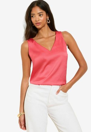 V-neck sleeveless top in vibrant coral satin fabric, paired with white trousers. Features smooth texture and tailored fit.