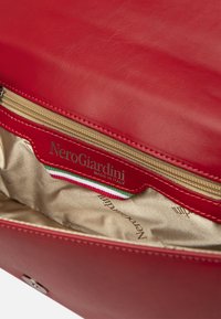 Sac à main en cuir rouge avec une fermeture éclair dorée, une doublure en satin beige et un logo embossé. Comprend un détail accent en tricolore italien.