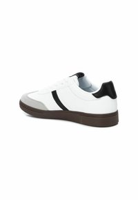 Zapatilla blanca con cap toe de ante gris, raya negra y acento negro en el talón; cuenta con una suela de goma texturizada y un diseño clásico de cordones.
