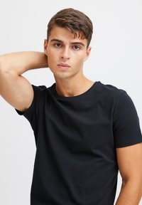 Maglietta nera a maniche corte con scollo a girocollo, realizzata in tessuto morbido. Texture liscia, design aderente, senza motivi o loghi visibili.