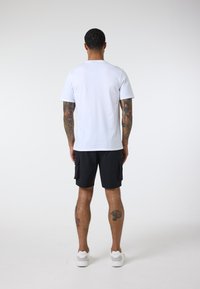White short-sleeve t-shirt with a round neckline, paired with black cargo shorts featuring side pockets. Worn with white sneakers.
