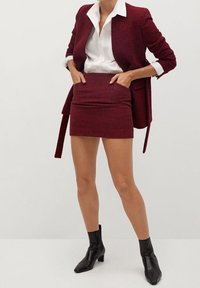 Blazer a quadri bordeaux abbinato a una mini gonna coordinata, con un design elegante e un tessuto testurizzato. Stivali neri alla caviglia completano il look.
