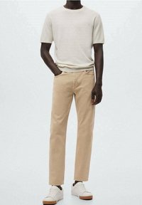 Pantalones de algodón beige combinados con una camiseta de manga corta blanco roto, completados con zapatillas blancas con suelas marrones. Diseño simple y moderno.