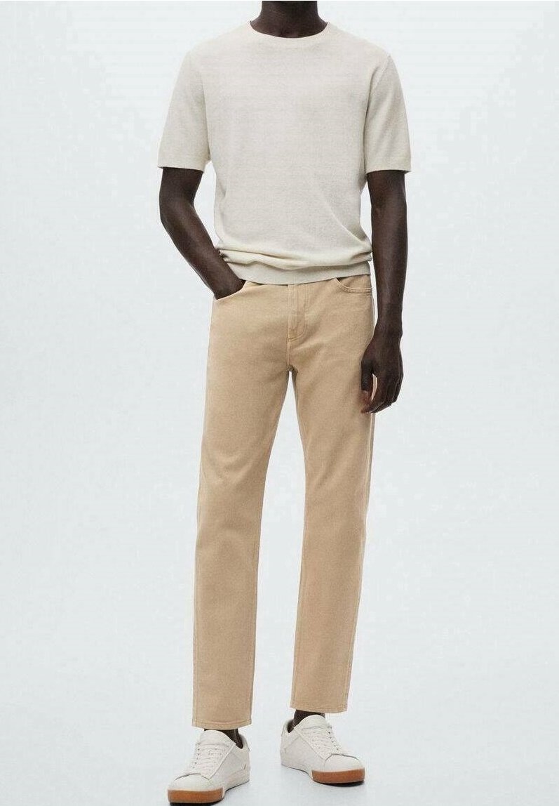 Pantalones de algodón beige combinados con una camiseta de manga corta blanco roto, completados con zapatillas blancas con suelas marrones. Diseño simple y moderno.