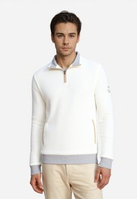 Weißer Pullover mit halbem Reißverschluss aus strukturiertem Stoff, grauem Kragen und Bündchen sowie seitlichen Taschen. Passt gut zu hellbeigen Hosen.