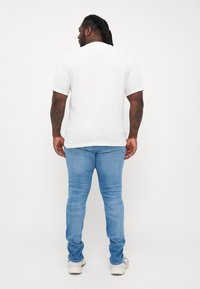 Biela tričko s krátkym rukávom a okrúhlym výstrihom skombinované so svetlomodrými slim-fit džínami. Hladká textúra a jednoduchý dizajn, pohľad zozadu.