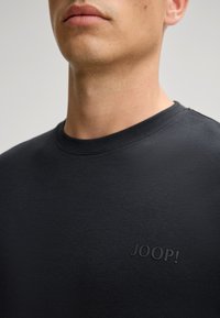 Zwarte katoenen T-shirt met een ronde hals en korte mouwen, voorzien van een subtiele reliëfprint van het logo "JOOP!" op de borst. Soepele textuur.