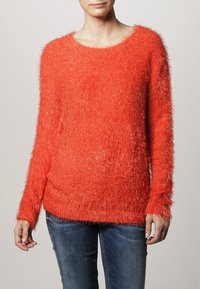 Klart orange fluffig tröja med långa ärmar, rund halsringning och en lös passform, med ett mjukt, texturerat material.