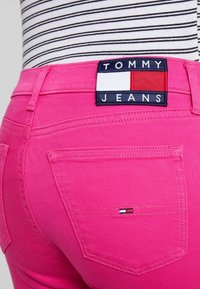 Růžové džíny s těsným střihem, které mají štítek Tommy Jeans na pase a malou nášivku s logem na zadní kapse.