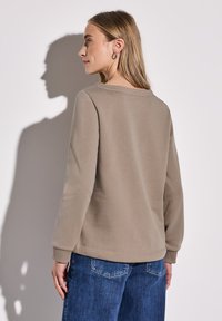 Felpa marrone con collo a giro e maniche lunghe, abbinata a jeans in denim blu. Tessuto morbido e dettagli con polsini a coste. Design semplice e minimal.