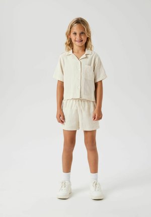 Lichtbeige katoenen tweedelig outfit met een knoopsluiting, kort trainlongtop met zak en bijpassende shorts met elastische tailleband.
