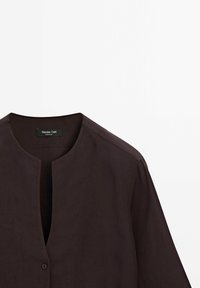 Blouse marron foncé à manches longues avec un col rond et une fermeture à un bouton, présentée sur un fond blanc.