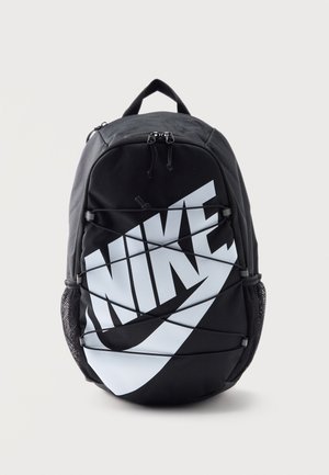 Sac à dos Nike noir avec grand logo blanc, cordon élastique à l’avant, poches latérales en mesh et compartiment principal à double fermeture éclair.