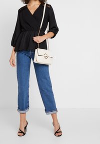 Black peplum blouse with lace accents, paired with rolled-up blue jeans and black strappy heels. White handbag with gold hardware.