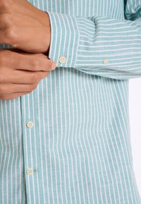 Lichtblauw en wit gestreept shirt met een knoopmanchet. Heeft een zachte textuur en een subtiele glans, gemaakt van een lichte stof.