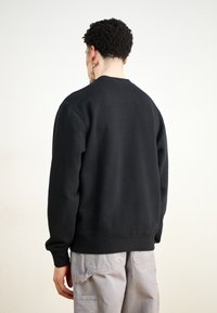 Sudadera de forro polar negra con cuello redondo, puños y dobladillo acanalados, con una textura suave y un corte holgado, combinada con pantalones cargo grises.