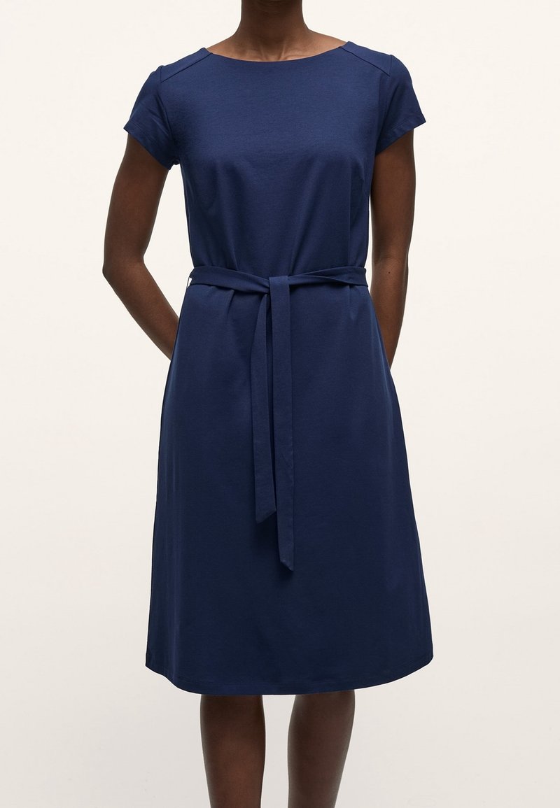 Robe bleu marine en tissu doux, dotée de manches courtes, d'un col rond et d'une ceinture à nouer à la taille pour définir la silhouette.