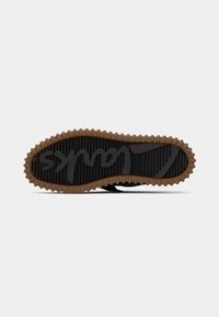 Semelle de chaussure avec une bande de roulement épaisse marron entourant une base noire, présentant le texte en relief "Clarks" et le logo au centre.