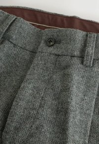 Gray tweed trousers featuring a textured weave, a button closure, and a contrasting brown waistband lining.