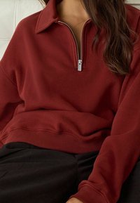 Bordeauxrode trui met een ritskraag, voorzien van een geribbelde zoom en manchetten. Gemaakt van zachte stof, met een gladde textuur en een losse pasvorm.