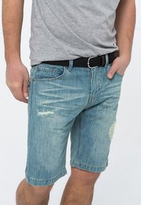 Lyseblå denimshorts med slidte detaljer og frynset kanter, der har et klassisk fem-lomme design og et sort vævet bælte.