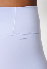 Heledad lillasest kõrge vöökoha ja siledaga retuusid. Omab "AEROREADY" logo vöökoha lähedal ja kontrastset õmblemise detailide.