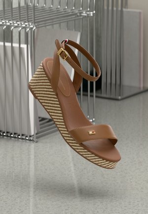 Sandalias marrones de cuña con una plataforma tejida texturizada, que presentan una amplia correa frontal, una correa para el tobillo con una hebilla dorada y un acento decorativo de logo.